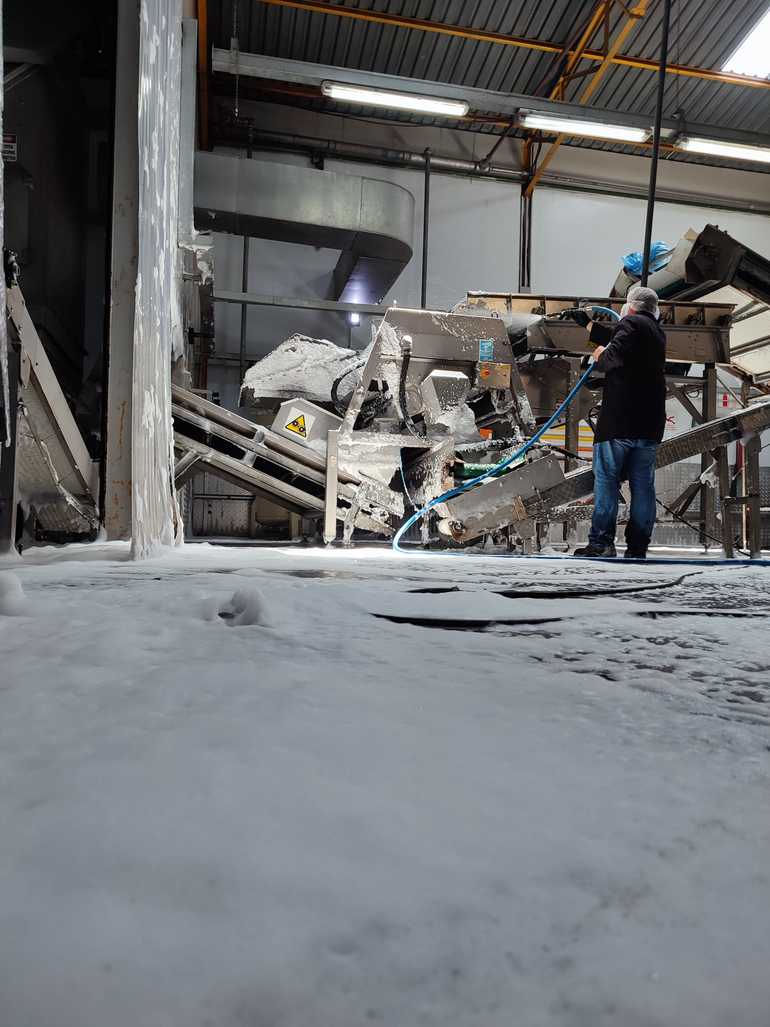 FactoryFresh team member using a cleaning lance beside foam-covered production equipment